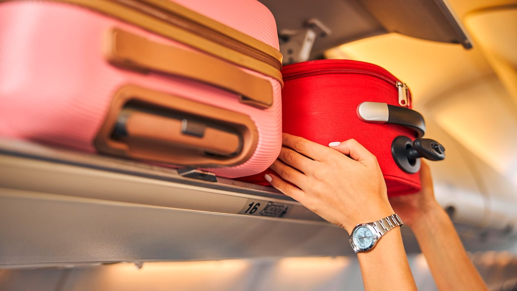 Extragebühren fürs Handgepäck sollen fallen 2D80JFB Hands laying down a carry-on baggage on an upper shelf