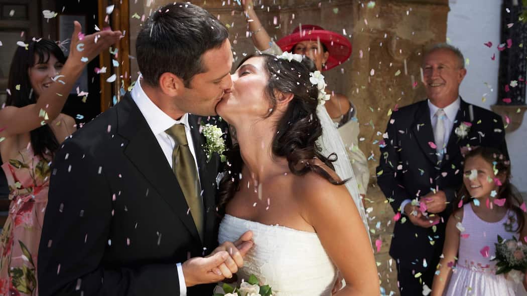 Lohnt es sich zu heiraten? Ein frisch vermähltes Paar küsst sich an seiner Hochzeitsfeier.