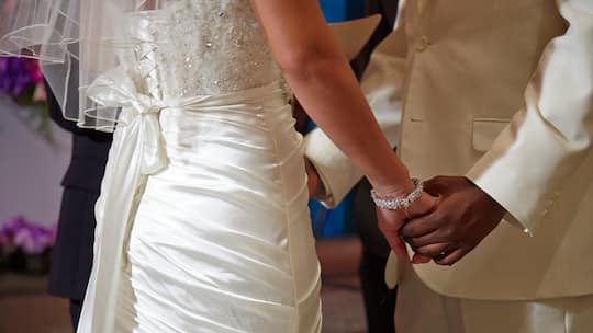 Ein frisch verheiratetes, binationales Ehepaar hält sich an den Händen.