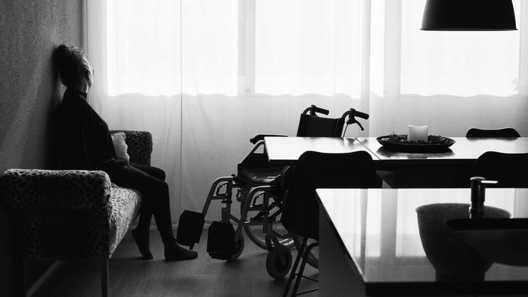 Den Betroffenen geht das Geld aus Anonyme Frau sitzt auf einem Sofa, vor ihr ein Rollstuhl. Auch zwei Jahre nach der Infektion leiden manche noch an Long Covid. Ihr Taggeld wird eingestellt, die IV lässt sich Zeit – jetzt kommt zur körperlichen noch die finanzielle Not.