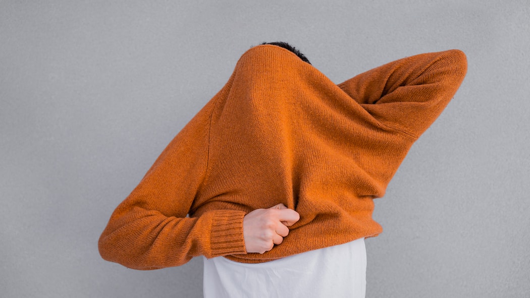 «Intuition hilft uns, rasch zu entscheiden» Unrecognisable man pulling cozy caramel sweater over his head on grey background. He is also wearing white t-shirt.