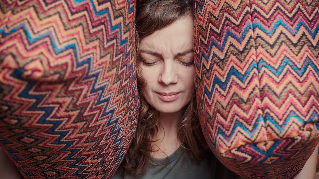 So krank macht uns ständiger Lärm Frau hält sich die Ohren mit Kissen zu - Der Alltagslärm nimmt zu – darunter leiden hochsensible Menschen besonders. Aber auch der Rest der Bevölkerung