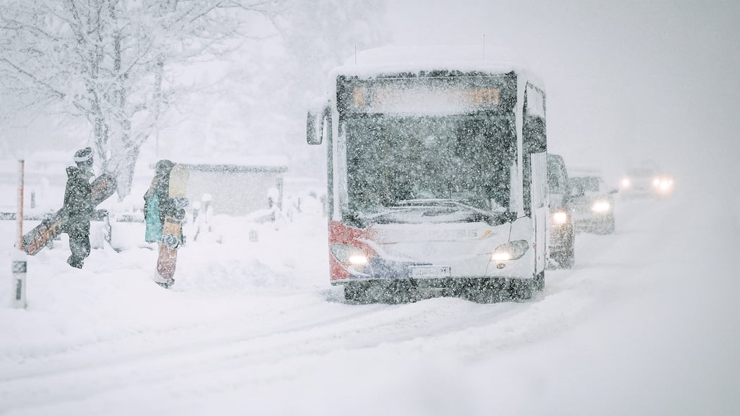 Geld zurück, wenn das Wetter die Ferien vermiest? Bus im Schneegestöber. Snowboarder steigen ein.