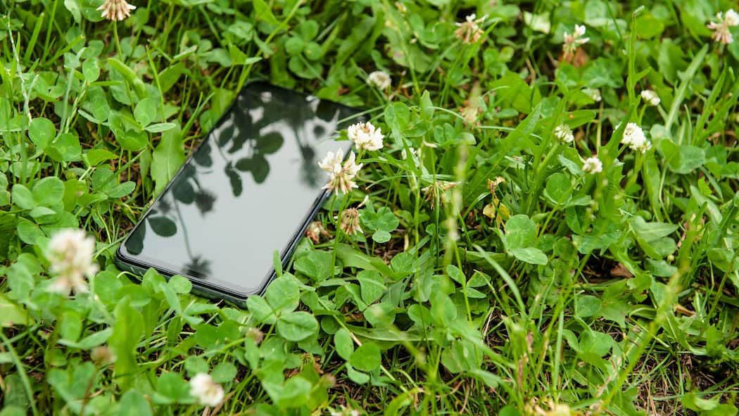 So finden Sie ein verlorenes Handy auch ohne Internet Ein Smartpohne liegt mitten in einer Wiese, vom Gras halb verdeckt.