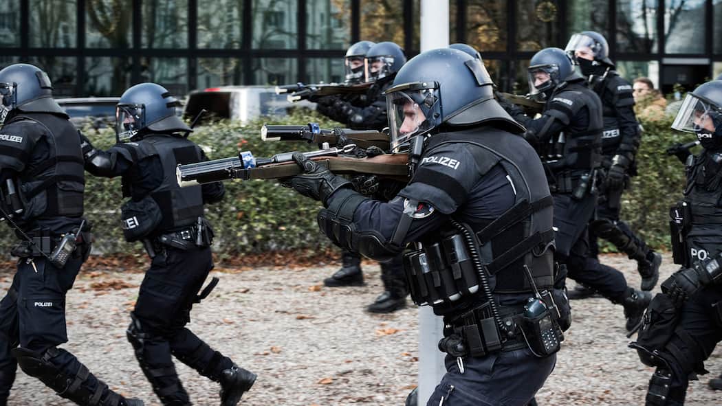 Verfahren gegen Basler Behörden soll eingestellt werden Polizisten rennen mit erhobenen Gummischrot-Gewehren im Anschlag und in schwarzer Vollmontur mit Helm durch einen Park.