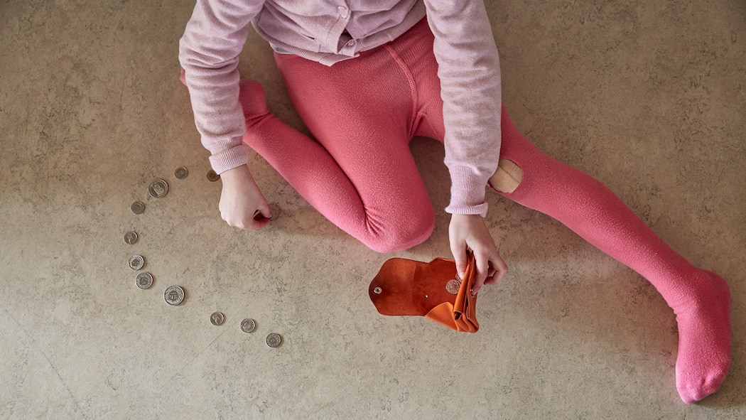 Die Sozialhilfe für Kinder reicht nicht aus Ein Mädchen in pinken Strumpfhosen sitzt auf dem Boden, in den Händen ein fast leeres Portemonnaie. Auf dem Boden vor ihr hat sie einige Geldmünzen ausgebreitet.
