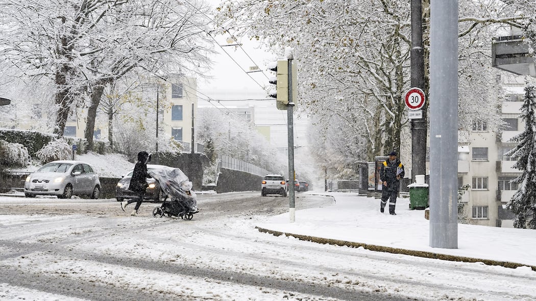 Zu spät im Büro – muss ich länger arbeiten? Eine Person überquert mit einem Kinderwagen die verschneite Strasse in Lausanne. Müssen Arbeitnehmerinnen und Arbeitnehmer länger arbeiten, wenn sie wegen des Schnees und vereister Strassen zu spät zur Arbeit kommen?