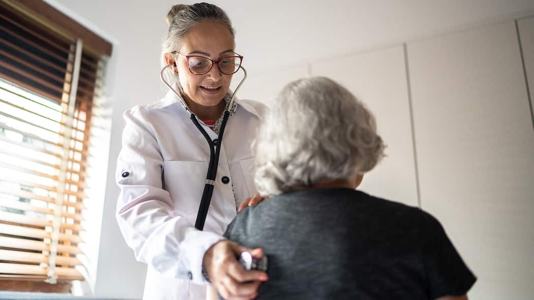 Krankenkassenmodell wechseln: Das geht jetzt jederzeit Doctor using stethoscope to exam senior woman at home