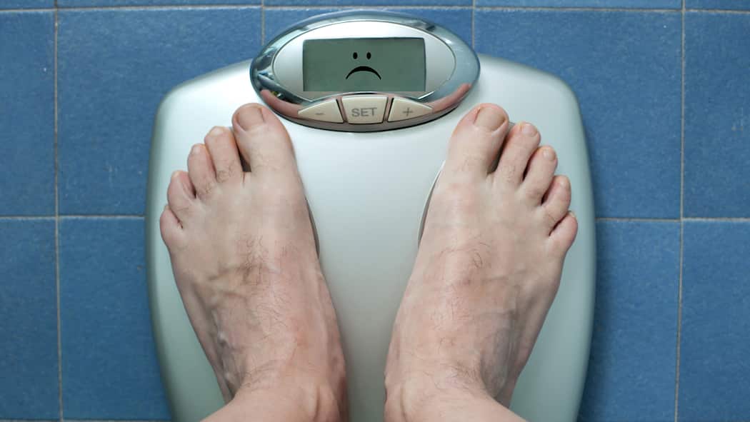 So gesund ist Intervallfasten wirklich Zwei Männerfüsse auf einer Waage, die einen traurigen Emoji anzeigt. Warum Intervallfasten nicht so gesund ist wie man denkt.