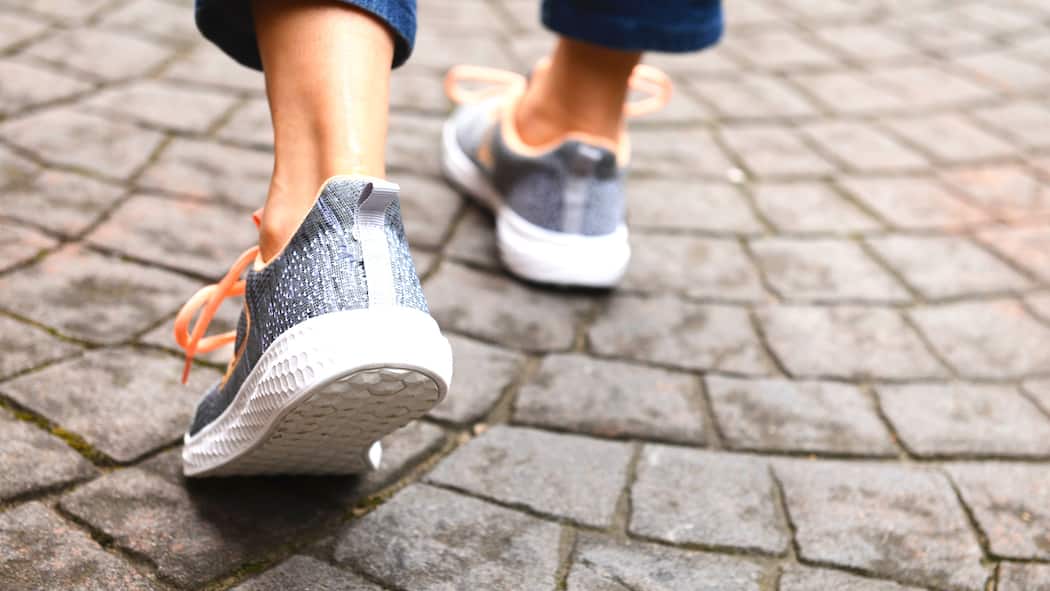 Mit 4000 Schritten pro Tag bleiben Sie länger fit Ein Mensch geht über Pflastersteine. Man sieht nur die Füsse von hinten. Sie stecken in Turnschuhen