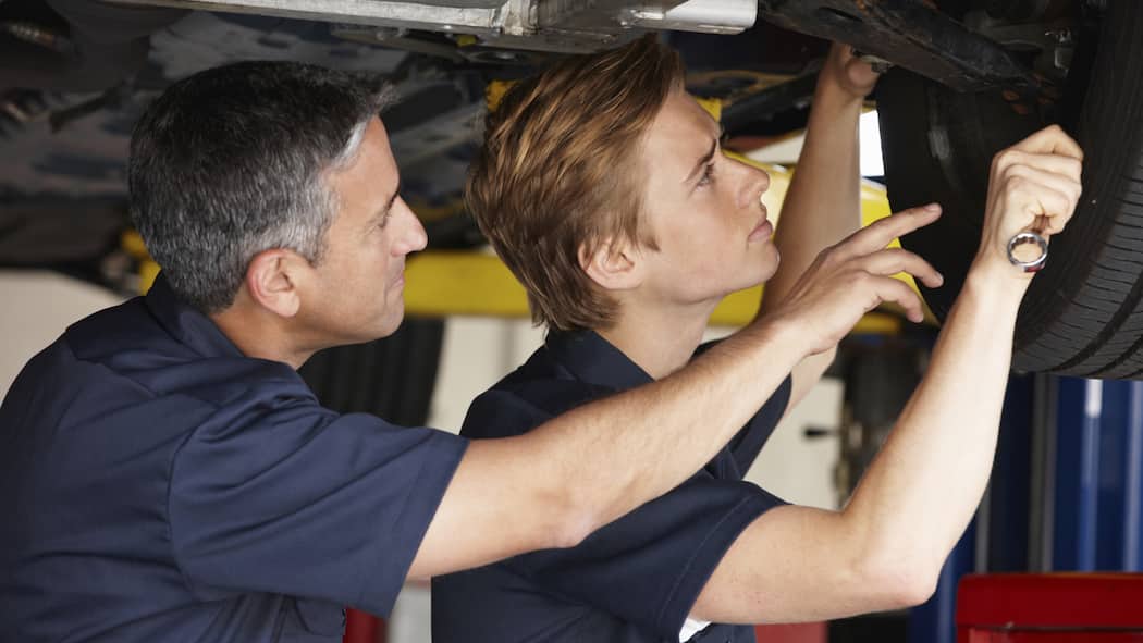 Zufrieden mit deiner Stifti? Ein Auto steht auf einer Hebebühne während zwei Mechaniker eine Inspektion durchführen.