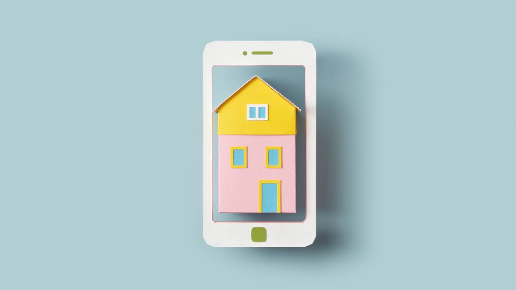 So erkennen Sie Fake-Angebote auf Buchungsplattformen Ein Handy mit einem Haus darin vor blauem Hintergrund. Nicht selten kommt es zu einem Betrug auf den verschiedenen Vergleichsplattformen.