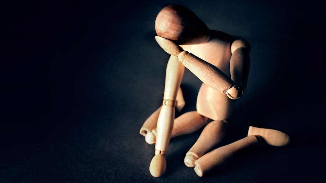 So gehen Sie mit der Invalidenversicherung um Eine Holzfigur kniet am Boden und hält verzweifelt seinen Kopf.