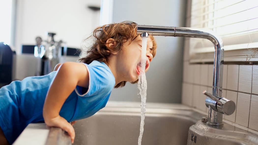 Woher kommt es? Wer überprüft die Qualität? Ein kleiner Junge lehnt sich über ein Spülbecken und streckt seinen Kopf zum Trinken unter den Wasserstrahl. Woher kommt eigentlich das Schweizer Leitungswasser und welche Anforderungen muss es erfüllen, damit wir es problemlos trinken können?