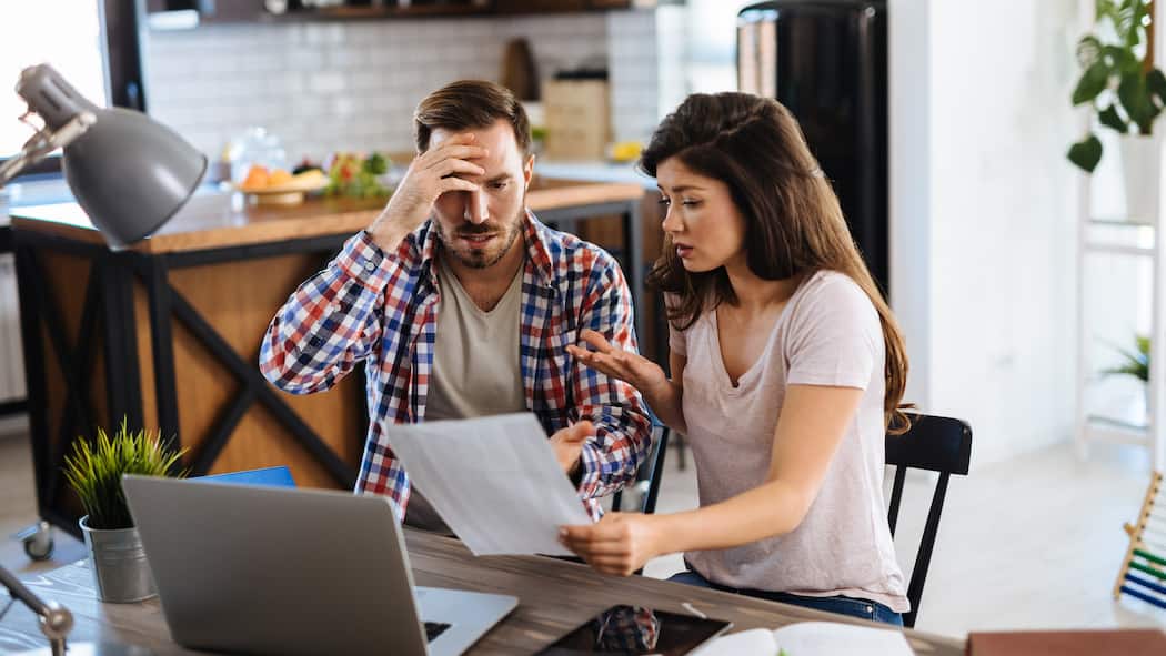 Haften Verheiratete immer gegenseitig? Ein Paar sitzt am Küchentisch und diskutiert mit besorgter Miene über offene Rechnungen.