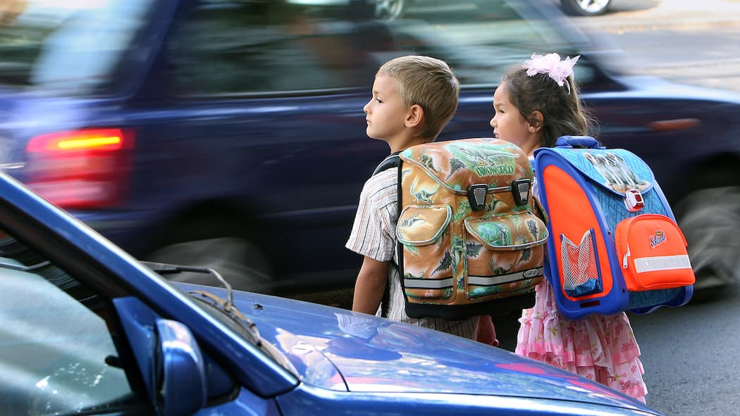 Der lange Kampf um sichere Schulwege Zwei Schulkinder stehen an der Strasse und wollen diese überqueren.