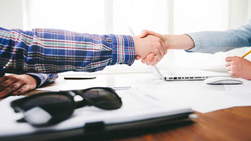 Hoppla, ist das jetzt ein Vertrag? Zwei Personen sitzen an einem Schreibtisch und geben sich zum Zeichen des Vertragsschlusses die Hand.