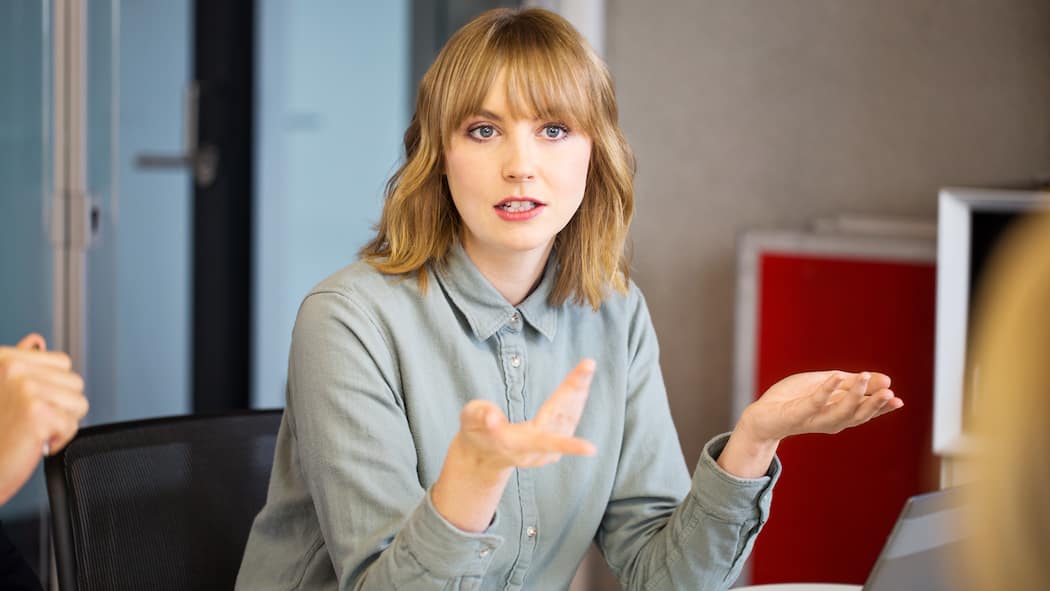 Ist es Zeit für eine Sanierung – oder für den Konkurs? Geschäftsfrau diskutiert an einem geschäftlichen Termin. Sie gestikuliert mit den Händen.