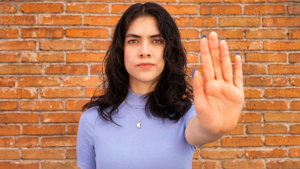 Sie sind nicht machtlos gegen Gewalt Eine junge Frau steht vor einer Mauer und streckt ihre Hand aus, mit der Handfläche Richtung Kamera.