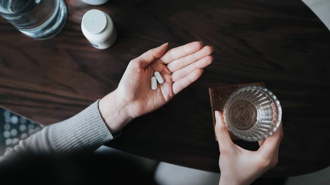 Was gegen Antidepressiva spricht – und was dafür Eine Frau hält in ihrer offenen Handfläche zwei Tabletten und in der anderen ein Glas Wasser. Was gegen Antidepressiva spricht – und was dafür