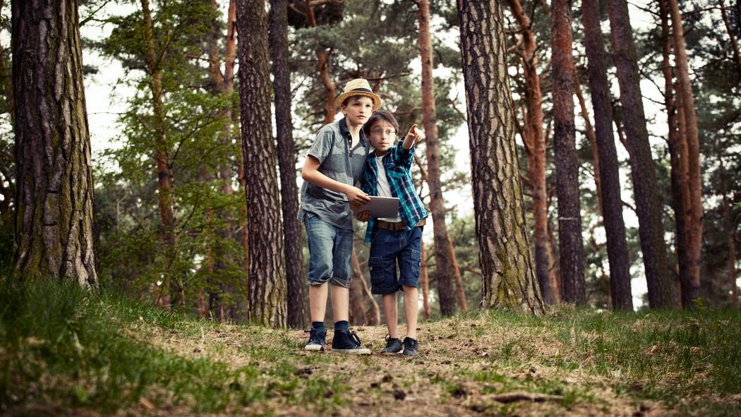 Jetzt aber nichts wie raus! Zwei Jungen stehen im Wald und halten ein Tablet in der Hand.