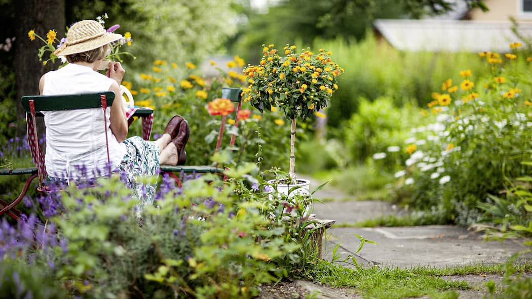 So sorgen Sie dafür, dass der Garten zu Ihnen passt Deutschland, Tee trinkende Seniorin sitzt am Tisch in einem sommerlichen Garten.