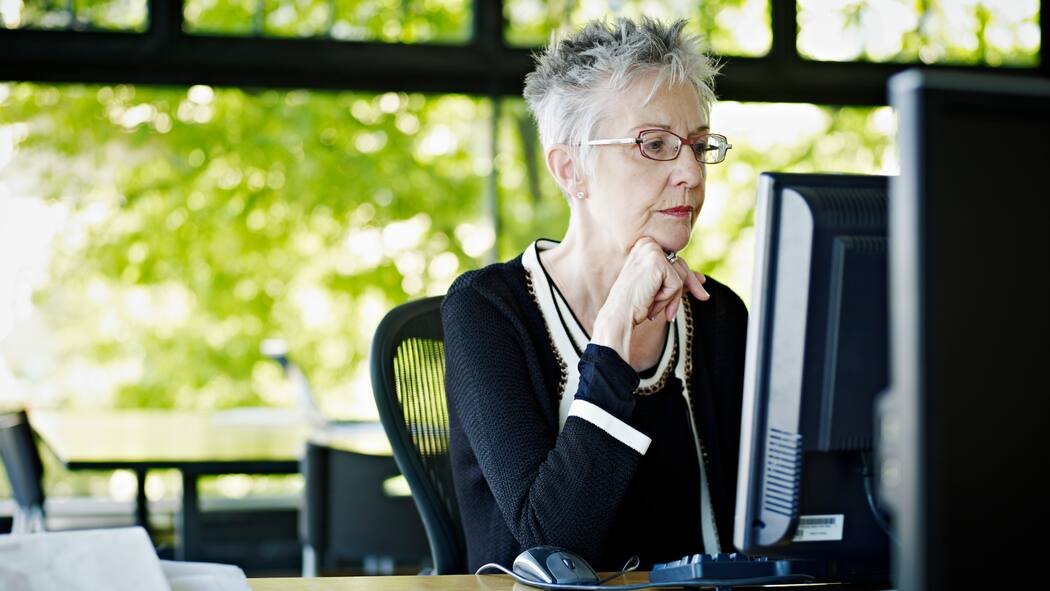 Können Frühpensionierte Arbeitslosengeld beziehen? Eine ältere Frau arbeitet im Büro am Computer.
