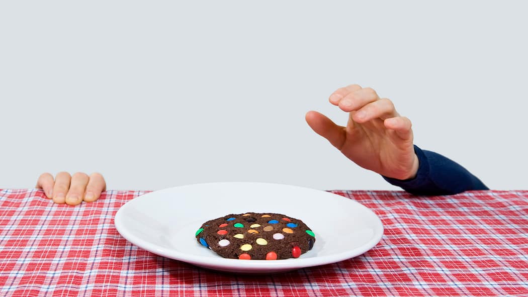 So setzen Sie Vorsätze endlich um Ein Mann versteckt sich unter dem Tisch und versucht, ein Cookie vom Tisch zu fischen.