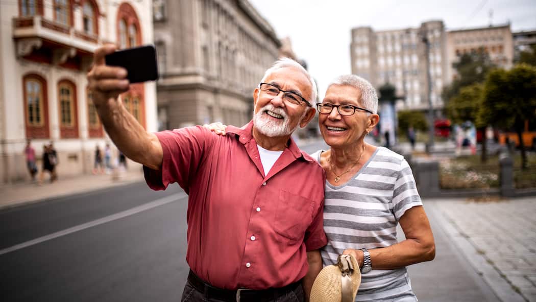 So haben Sie im Alter genug Geld Ein pensioniertes Paar in den Ferien macht ein Selfie auf einer breiten Strasse.