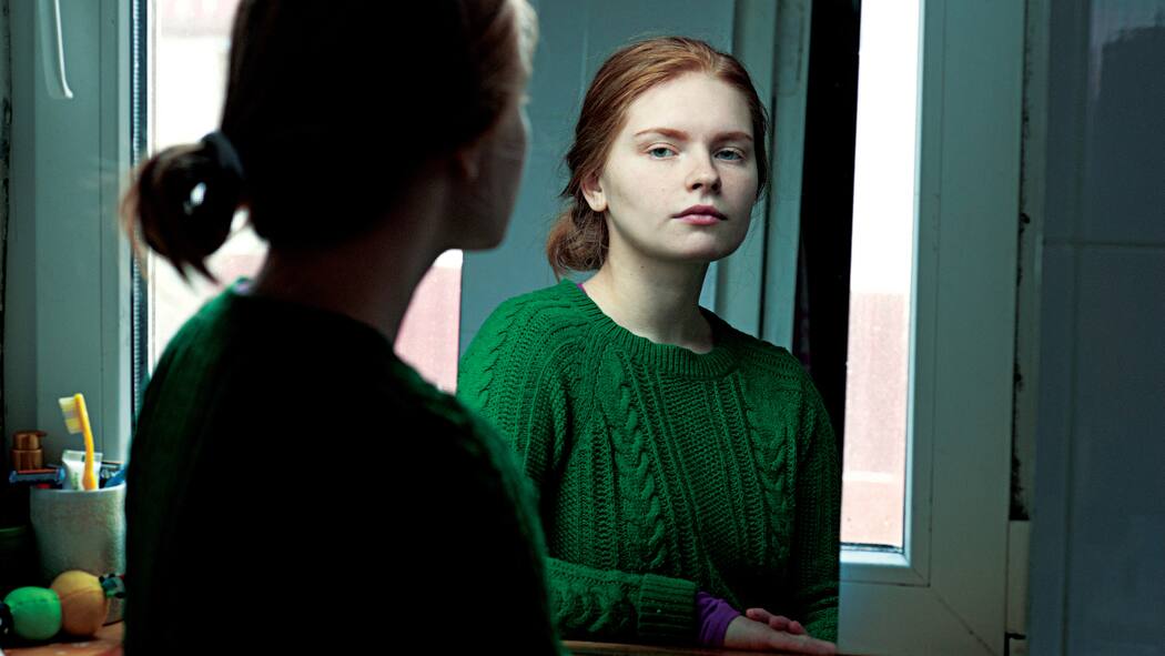 Wieso wir uns selber schlecht einschätzen können Eine junge Frau schaut sich im Spiegel an.
