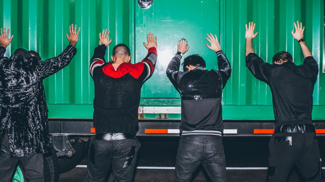 Welche Rechte Jugendliche gegenüber Uniformierten haben Vier Jugendliche stehen mit gespreizten Beinen und angelehnten Armen und Händen gegen eine grüne Containerwand, damit sie von der Polizei kontrolliert werden können.