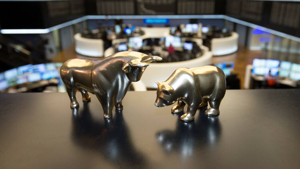 Ist jetzt die Zeit, um Geld anzulegen? Zwei goldigfarbene Spielfiguren in der Gestalt des Stiers (Aufwärtstrend) und des Bären (Abwärtstrend) stehen auf einer Unterlage in der Börse von Frankfurt, Deutschland.