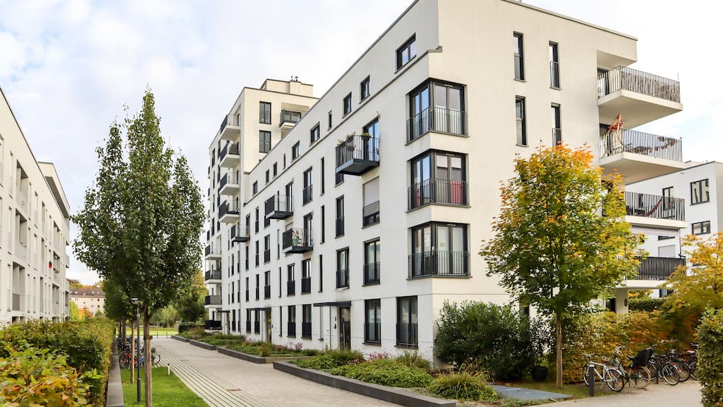 Welche braucht es? Moderne Wohnungen einer Stockwerkeigentümergemeinschaft mit Zugang über einen Gehweg umgeben von Bäumen.