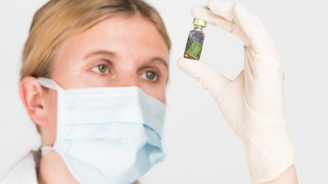 187,1 Millionen für Ärzte und Spitäler Eine Ärztin betrachtet eine Impfstoff-Flasche, die Notenscheine enthält.