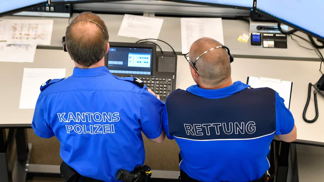 Haftet die Swisscom für Schäden? Zwei Beamte der kantonalen Notrufzentrale Aarau stehen vor mehreren Bildschirmen.