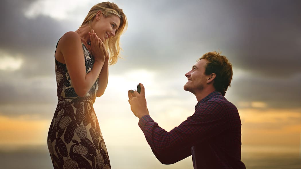 Was gilt rechtlich in der Ehe? Ein Mann macht einer Frau einen romantischen Hochzeitsantrag an einem Strand.