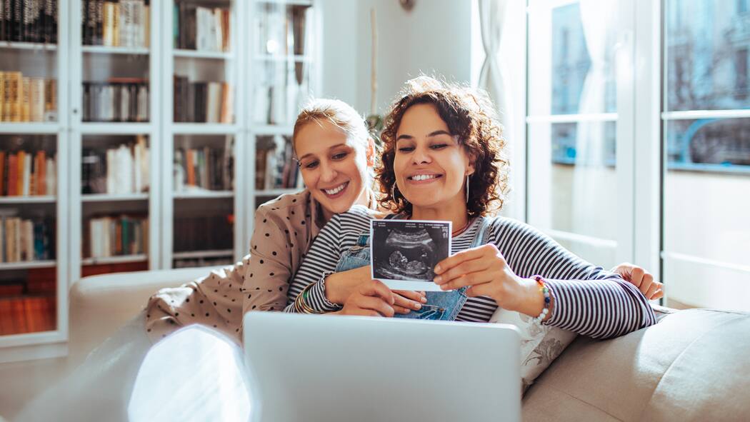 Einmal Einstein, bitte schön? Ein lesbisches Paar freut sich über die Schwangerschaft und hält ein Ultraschallfoto in eine Laptopkamera.