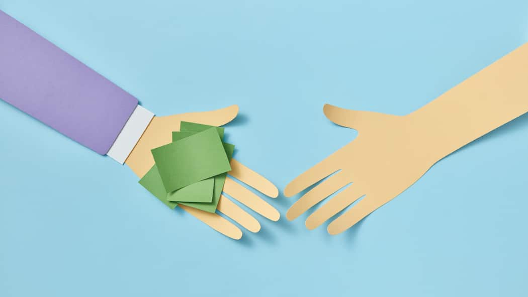 Freunden Geld pumpen: Darauf sollten Sie achten Eine Hand aus Papier gefaltet, überreicht einer zweiten Papierhand ein kleines Bündel mit Post-its, das sinnbildlich für Geld steht - Wer anderen ein Darlehen vermacht, sollte dies vertraglich festhalten, um die Rückzahlung des Privatdarlehens durch den Schuldner zu regeln.