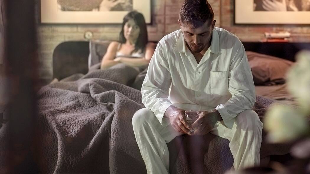Wenn der Ehepartner Alkoholiker ist Ein Mann mit einem Glas Whisky sitzt auf dem Bett und streitet sich mit seiner Frau.