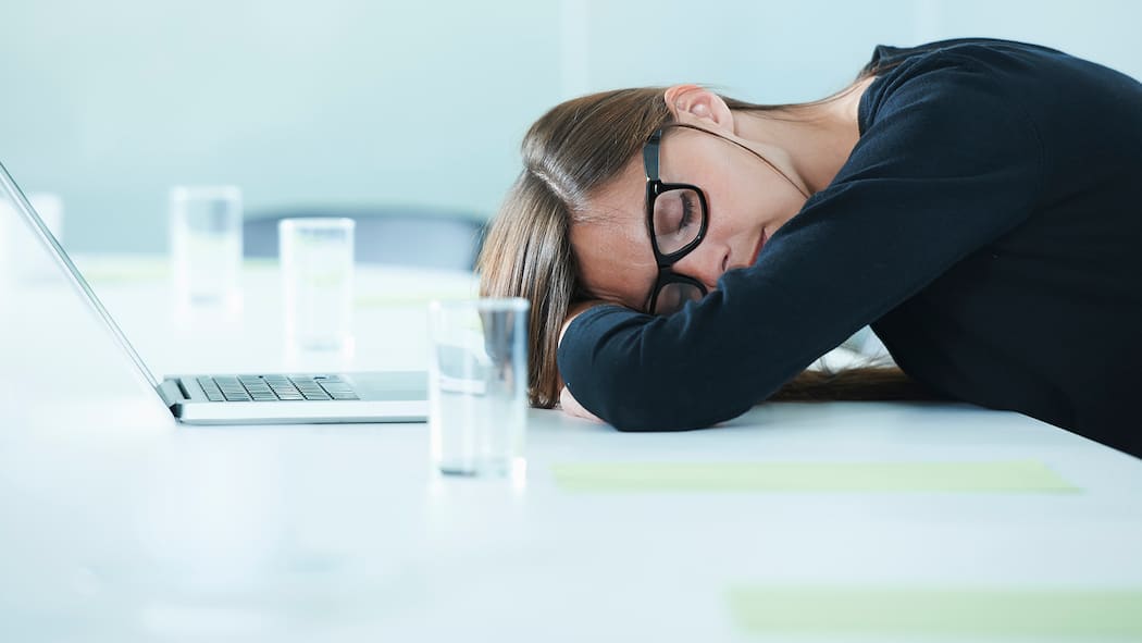 Der Büroschlaf ist der gesündeste Eine Frau macht im Büro ein Nickerchen.