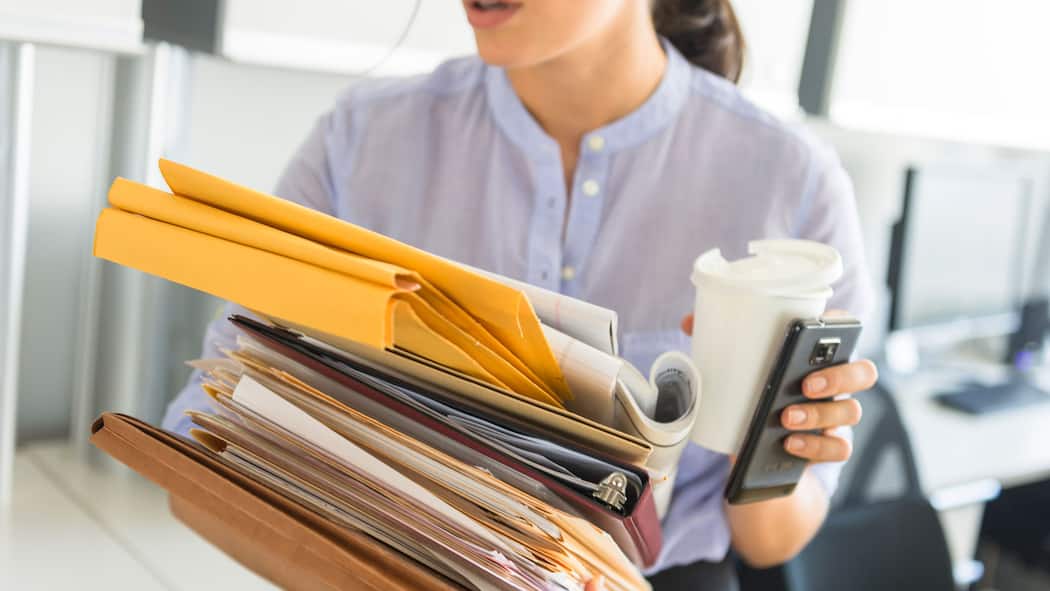 Keine Angestellten zweiter Klasse Eine gestresste Mitarbeiterin schleppt einen Stapel Dokumente in der einen Hand in der anderen einen Kaffeebecher und ein Handy