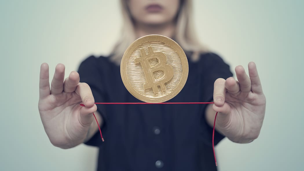 Wie erhalte ich das Geld zurück? Eine Frau balanciert eine Bitcoin-Münze auf einem Faden, den sie ausgestreckt in beiden Händen hält.
