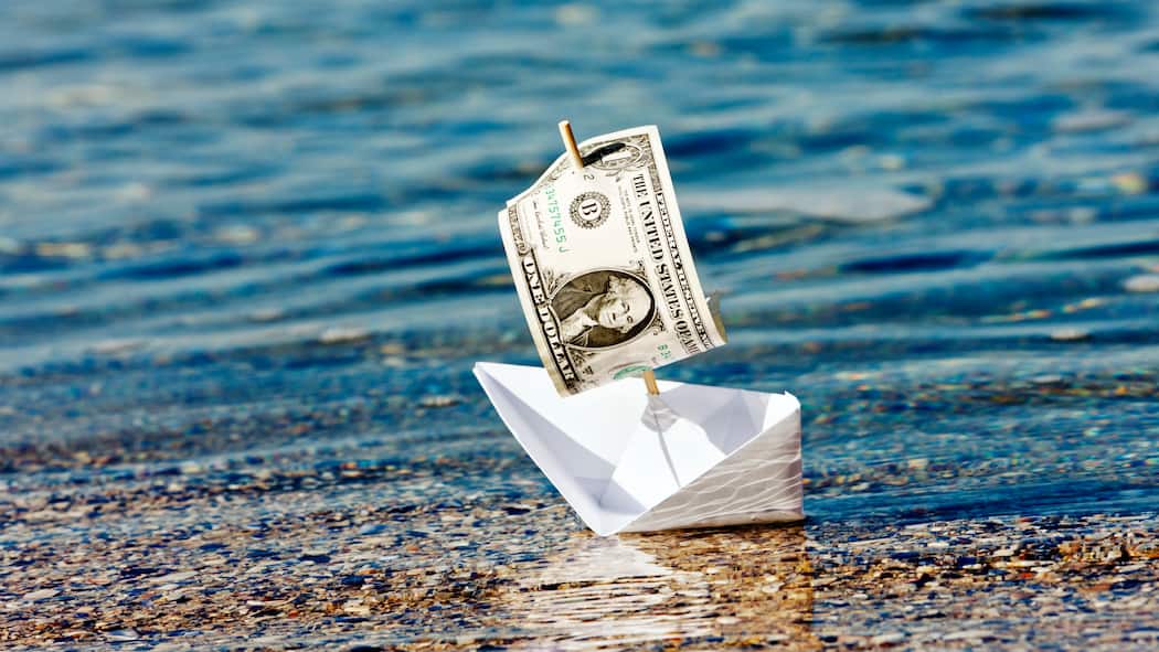 Sollen wir das Reisebüro betreiben? Ein Papierschiff mit einer Dollar-Note als Segel droht zu kentern und steht symbolisch für die USA-Rundreise, welche wegen der Pandemie storniert werden musste.