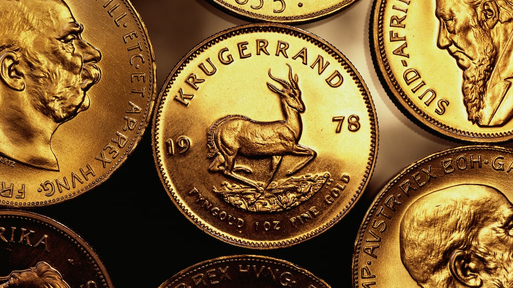 In Gold investieren – wie geht es am besten? Mehrere Krügerrand Goldmünzen liegen auf einer Oberfläche