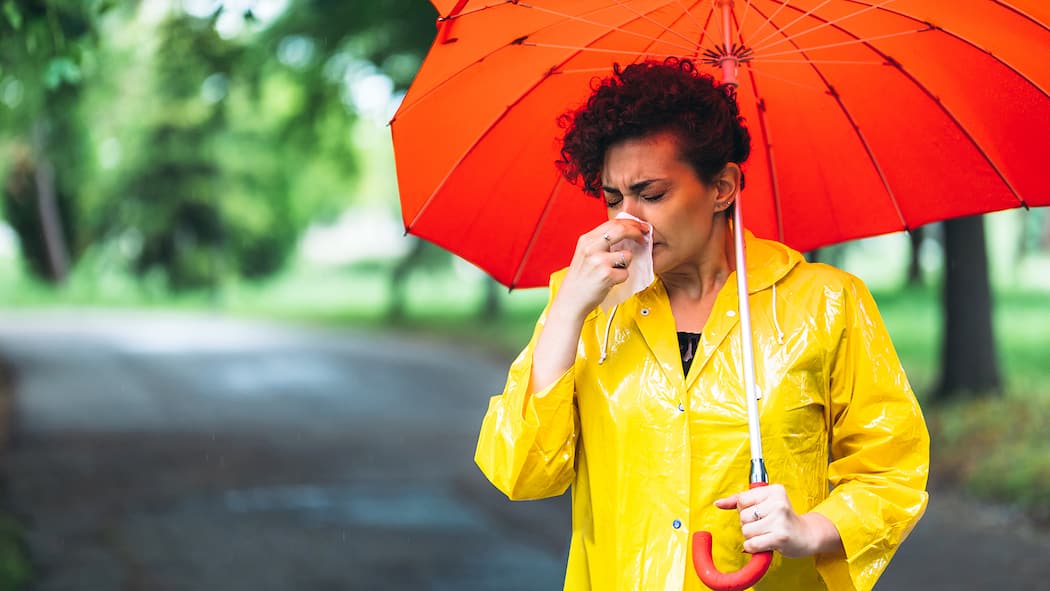 Was stärkt unser Immunsystem? Eine Frau mit gelbem Regenmantel schneuzt sich unter einem Schirm die Nase.