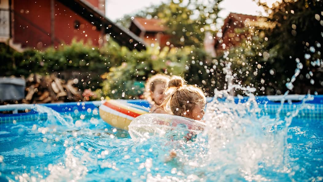 Pool-Party im Gemeinschaftsgarten – ist das erlaubt? Kleine Kinder plantschen vergnügt in einem aufgestellten Pool im Garten einer ruhigen Wohngegend.