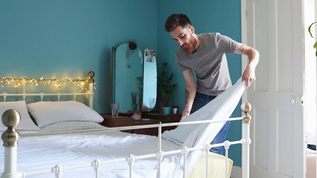 Wenn die Mitbewohner zum Problem werden Ein Mann schüttelt seine Bettdecke aus und richtet das Bett wieder her.