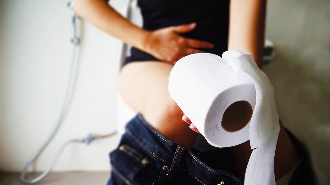 Was tun bei Blut im Stuhl? Eine Frau sitzt auf der Toilette und hält sich den Bauch.
