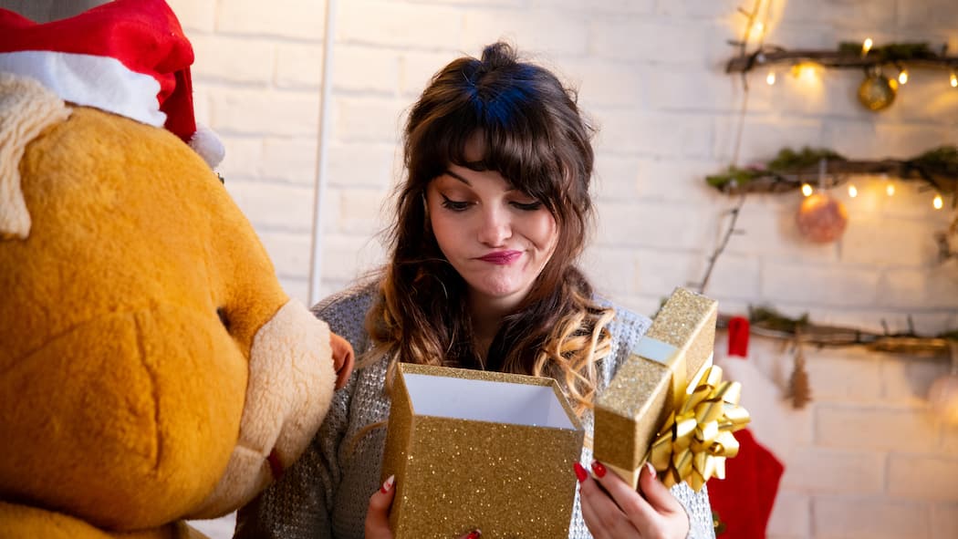 Vielen Dank für das Geschenk, aber ... Eine junge Frau öffnet ein verpacktes Weihnachtsgeschenk, schaut in die Box hinein und verzieht dabei die Mundwinkel. Wer zu Weihnachten etwas geschenkt bekommt, das nicht gefällt oder passt, kann das Präsent unter Umständen an den Händler zurückgeben oder es weiterverschenken.