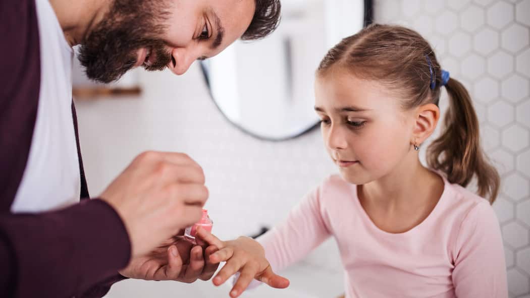 Wer zahlt wie viel bei alternierender Obhut? Ein kleines Mädchen hat ihre rechte Hand ausgestreckt, damit ihr Vater die Nägel lackieren kann.